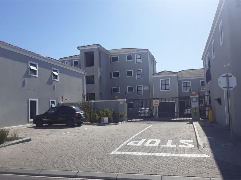 Exterior view of an apartment complex featuring a paved driveway, secure gated entrance, and dedicated parking bays.