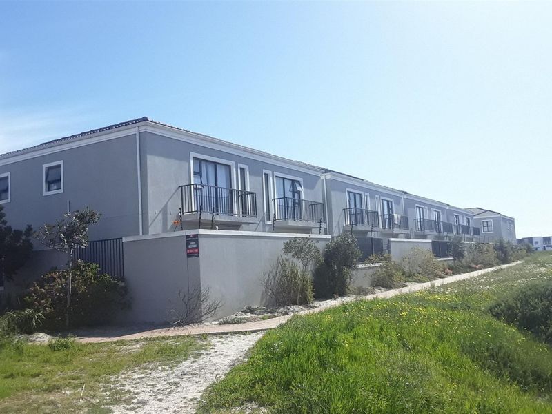 Rear elevation of a multi-unit apartment complex featuring private balconies, sliding glass doors, and perimeter security fencing.