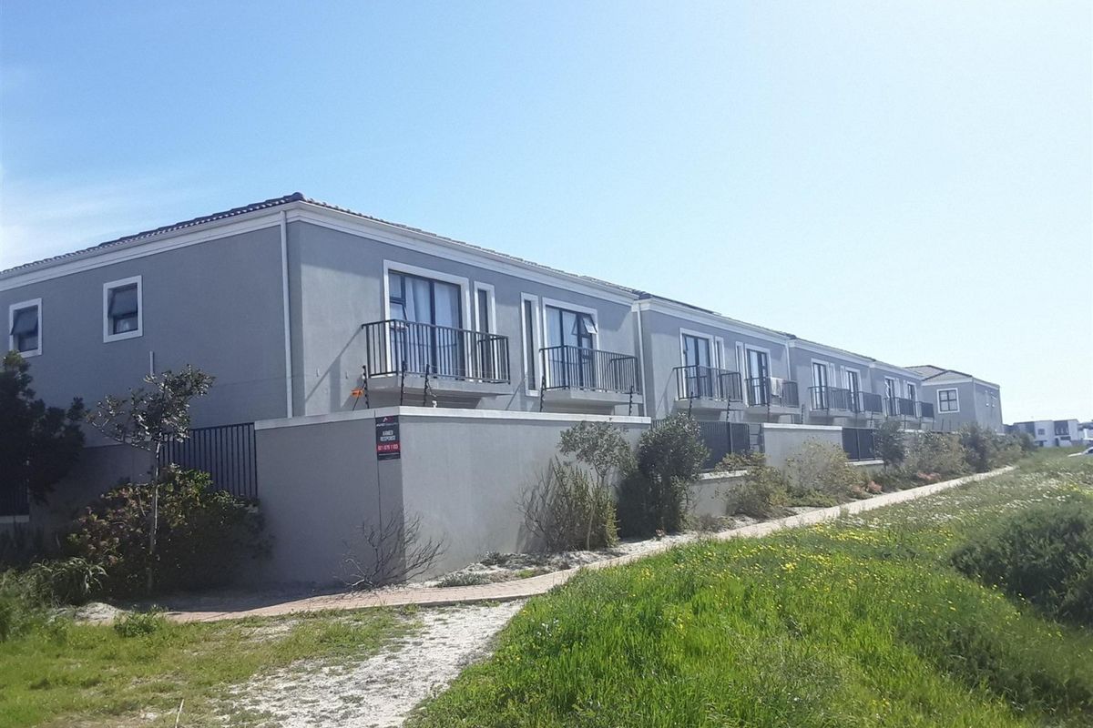 Rear elevation of a multi-unit apartment complex featuring private balconies, sliding glass doors, and perimeter security fencing.