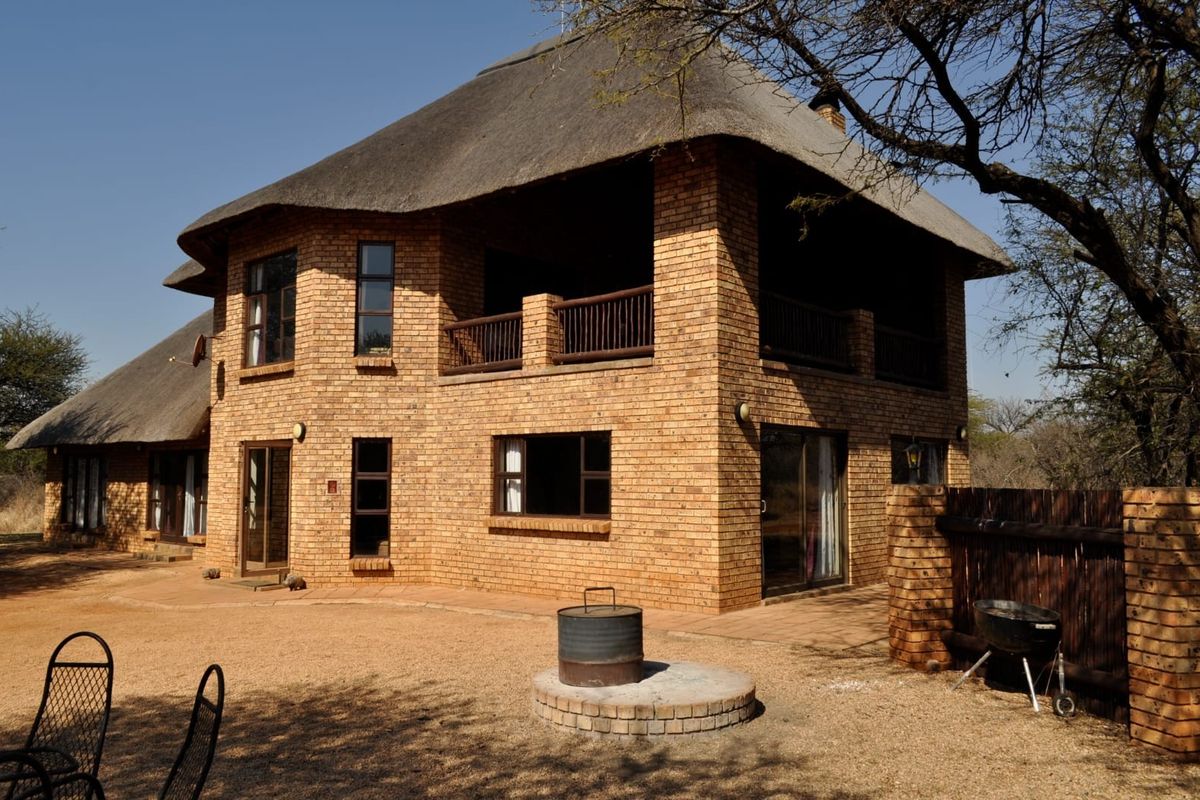 A two-story face brick house featuring a traditional thatched roof, an upper-level balcony, and a paved outdoor area with a built-in braai.