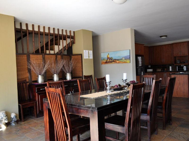 Spacious open-plan dining and kitchen area featuring stone tile flooring, wooden cabinetry, and a staircase with a decorative wooden balustrade.