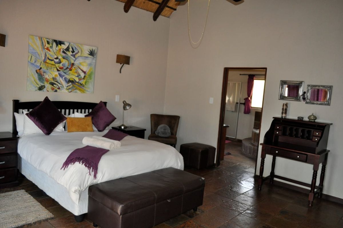 A spacious bedroom featuring exposed timber rafters, tiled flooring, and an adjoining en-suite bathroom.