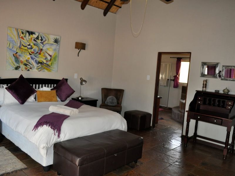 A spacious bedroom featuring exposed timber rafters, tiled flooring, and an adjoining en-suite bathroom.