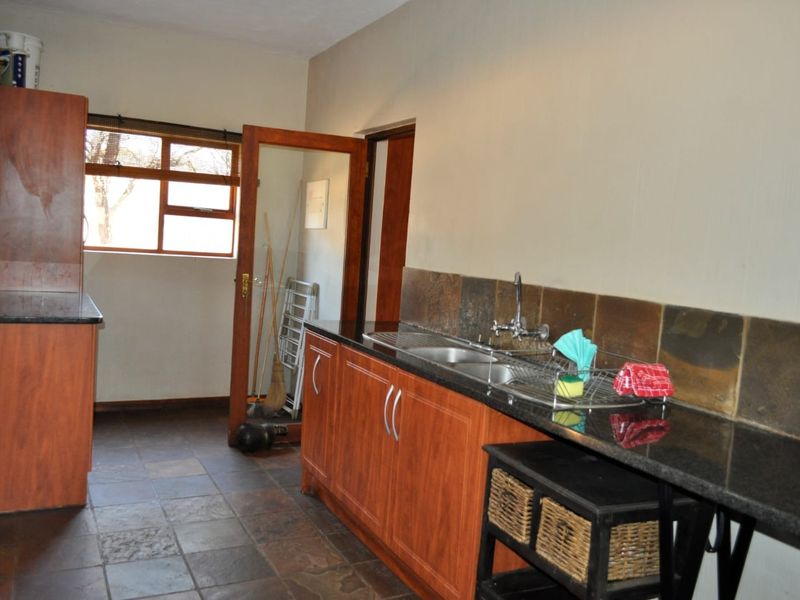 A functional scullery area featuring granite countertops, double sink, slate tile backsplash, and wood-look cabinetry with ample storage space.