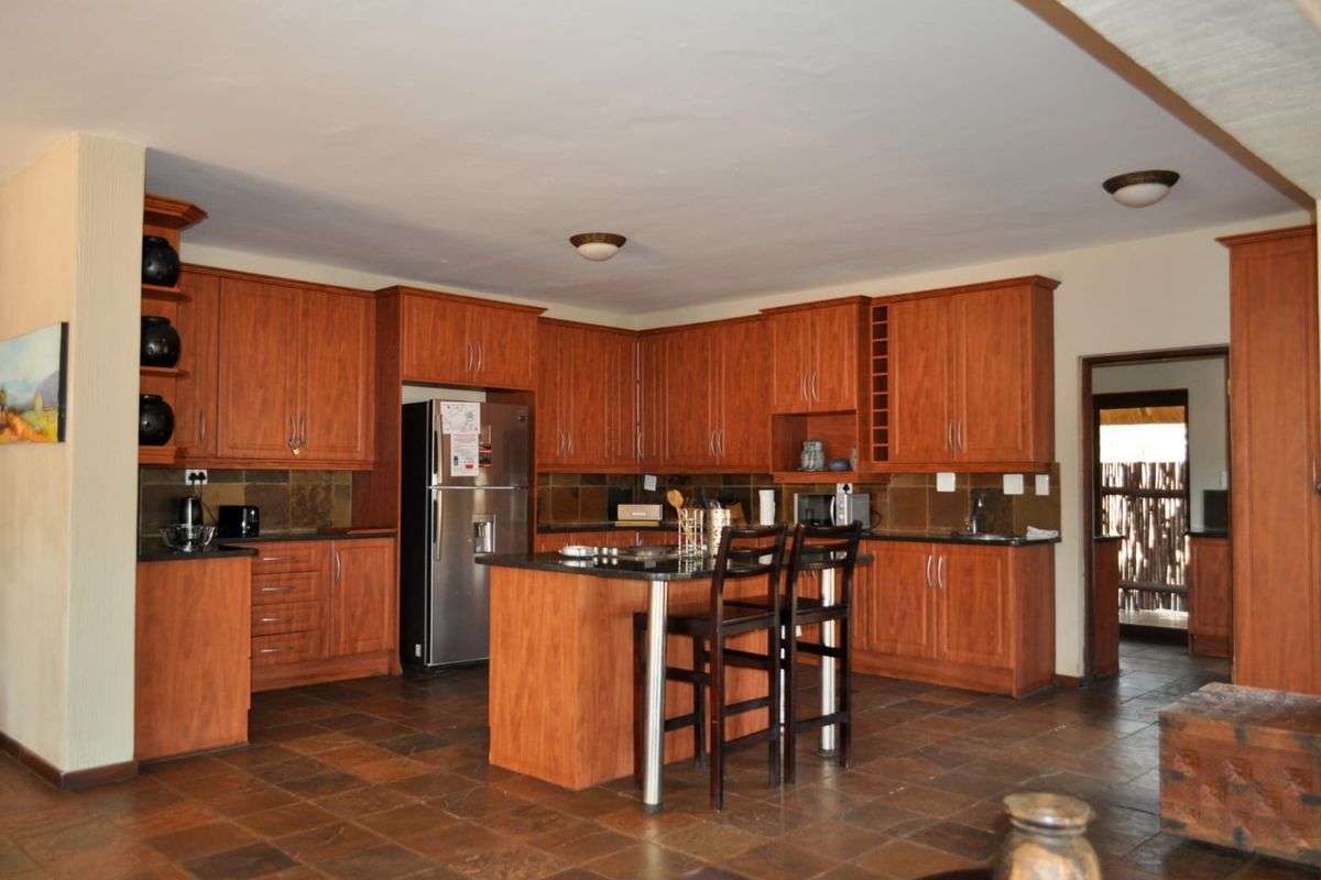 Spacious kitchen featuring warm-toned wooden cabinetry, granite countertops, a central island, and durable stone tile flooring.