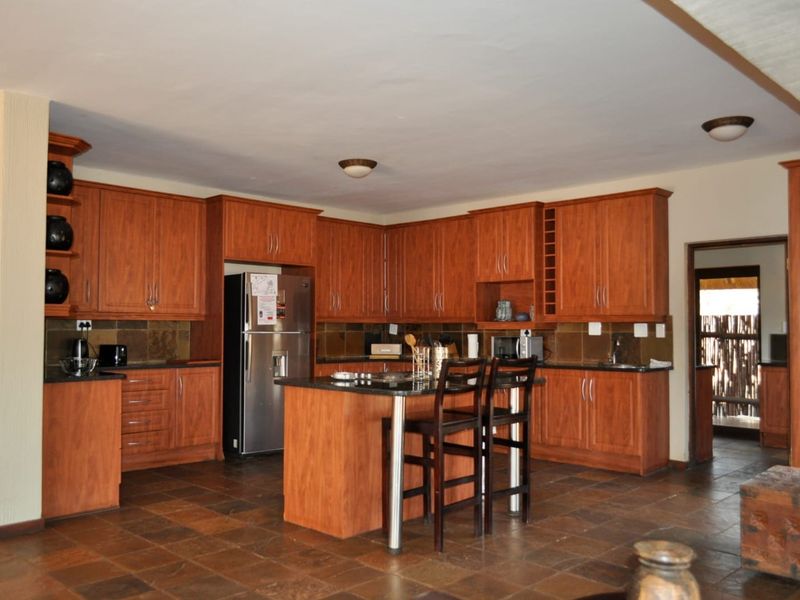Spacious kitchen featuring warm-toned wooden cabinetry, granite countertops, a central island, and durable stone tile flooring.