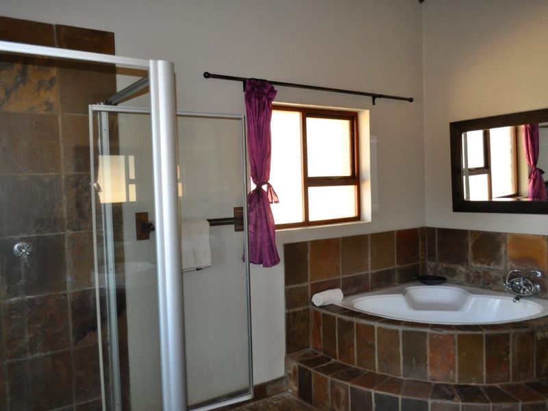 A bathroom featuring a corner bathtub with slate tile surround, a separate shower enclosure, and a wall-mounted mirror.