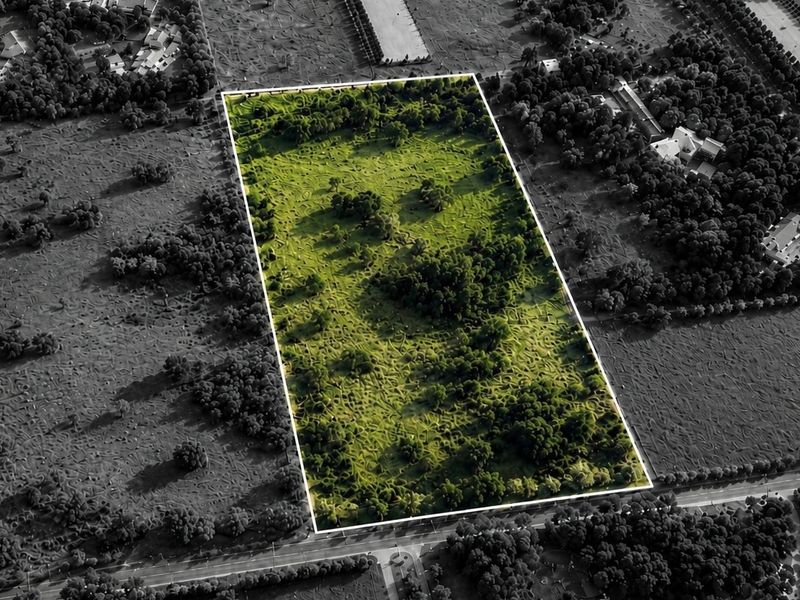 An aerial view of a rectangular vacant residential plot featuring established trees and natural vegetation, highlighted against the surrounding landscape.