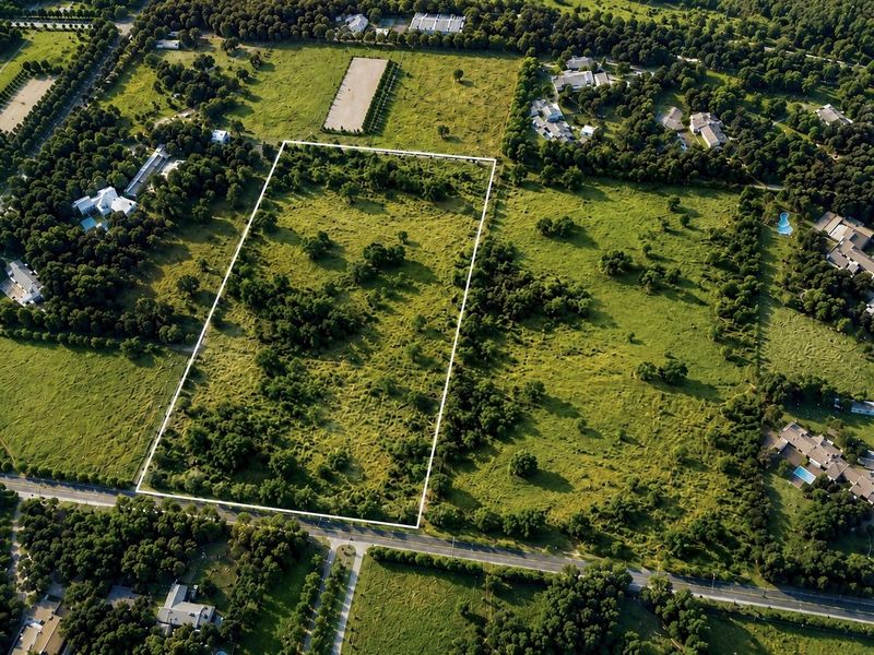 An aerial view of a large, undeveloped residential plot of land, clearly outlined with boundary markers, situated in a green, established neighborhood.