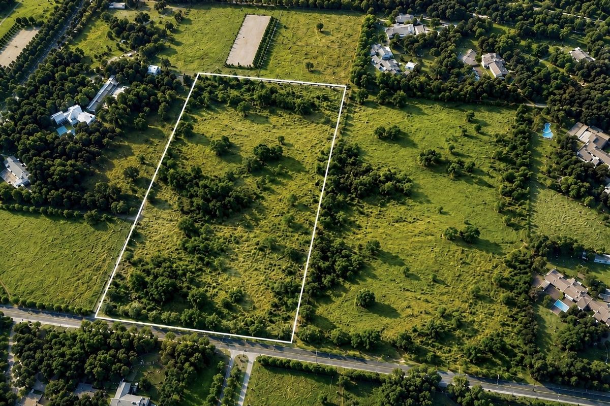An aerial view of a large, undeveloped residential plot of land, clearly outlined with boundary markers, situated in a green, established neighborhood.