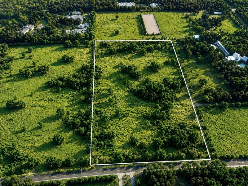 Aerial view of a large, rectangular vacant residential plot featuring lush green vegetation and mature trees, offering significant development potential.