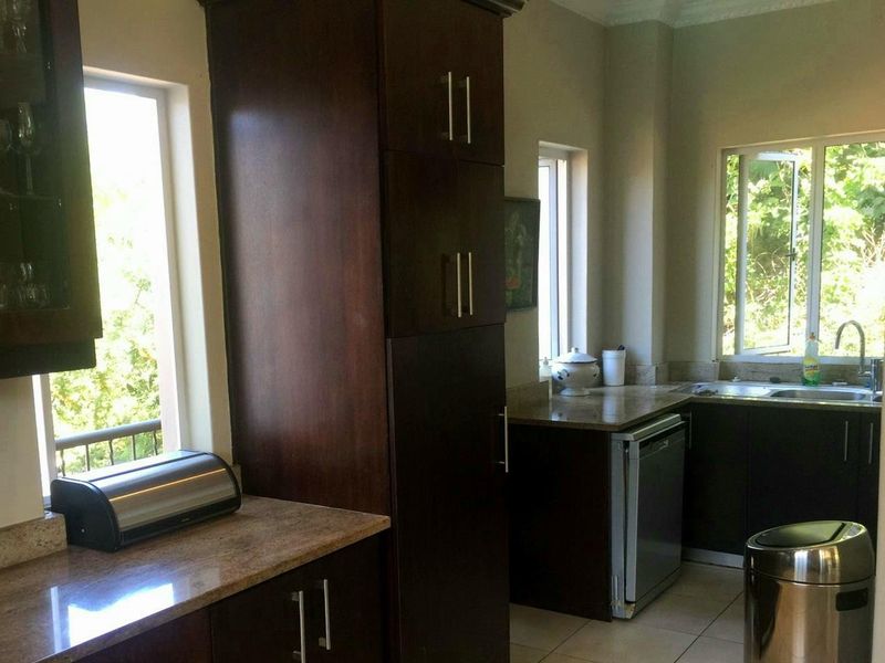 A functional kitchen featuring dark wood cabinetry, granite countertops, and a stainless steel sink, with natural light provided by multiple windows.