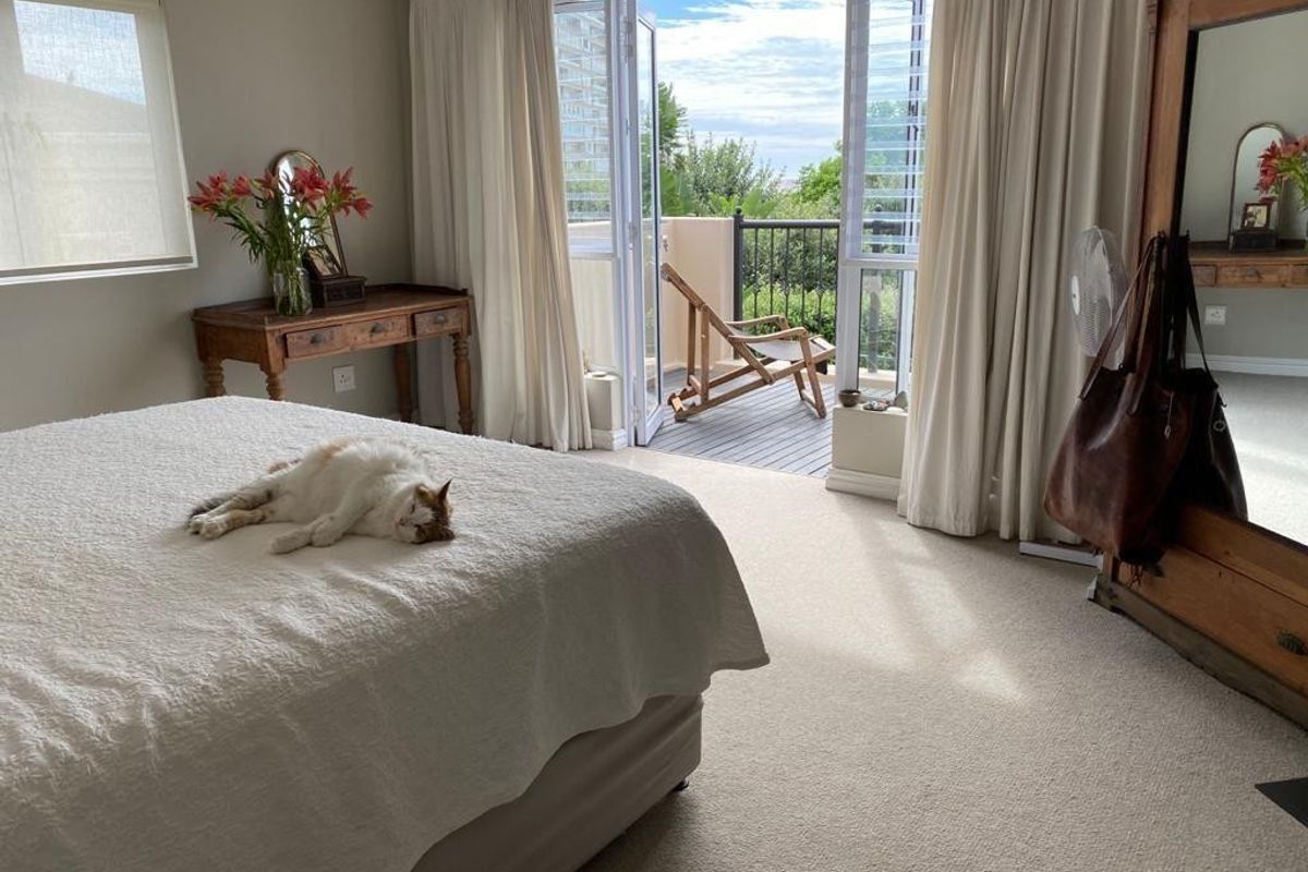 Spacious bedroom featuring neutral carpeting, large windows with roller blinds, and direct access to a private balcony through double glass doors.