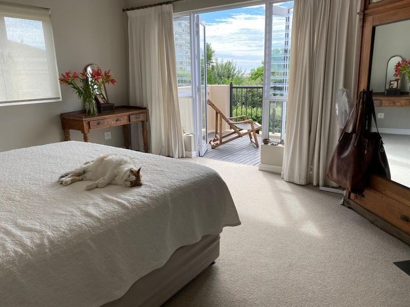 Spacious bedroom featuring neutral carpeting, large windows with roller blinds, and direct access to a private balcony through double glass doors.