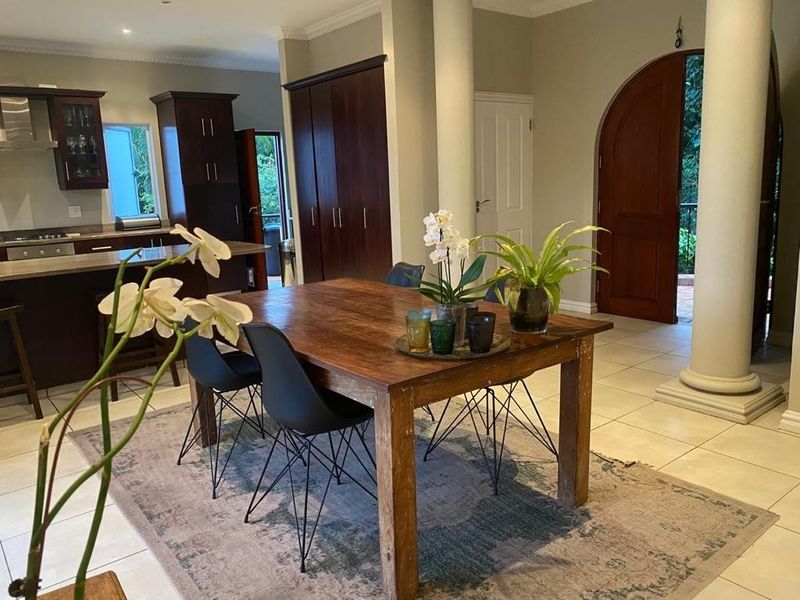 Open-plan living and dining area featuring a kitchen with built-in cabinetry, a central island, and direct access to an outdoor space through an arched door.