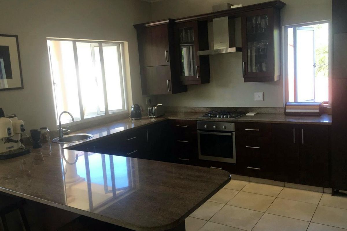 A functional kitchen featuring dark wood cabinetry, granite countertops, stainless steel appliances, and tiled flooring with ample natural light.