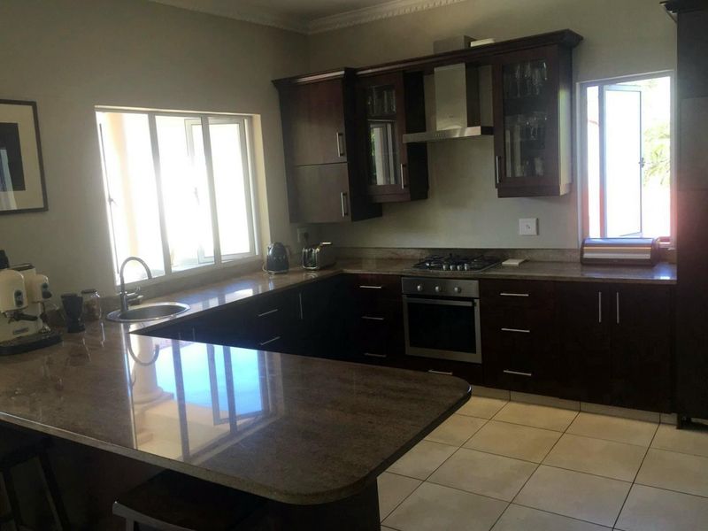 A functional kitchen featuring dark wood cabinetry, granite countertops, stainless steel appliances, and tiled flooring with ample natural light.