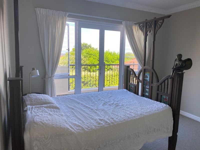 A well-lit bedroom featuring carpeted flooring, decorative cornice, and double doors providing direct access to a private balcony.