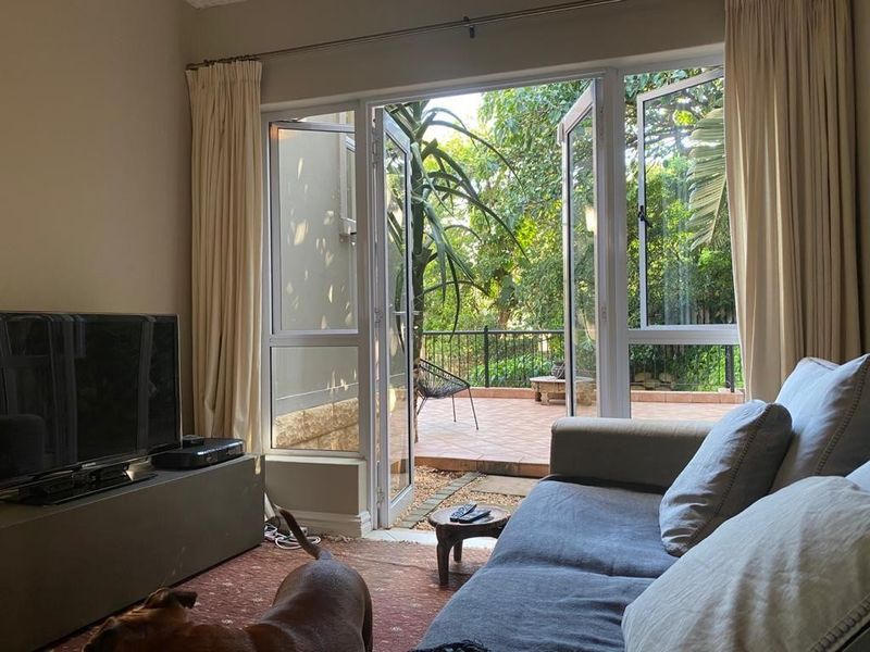 Living room featuring double glass doors opening onto a private tiled patio with garden views.