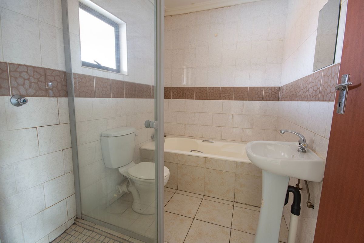 A dated bathroom featuring a pedestal basin, bathtub, and a glass-enclosed shower area with tiled finishes throughout.