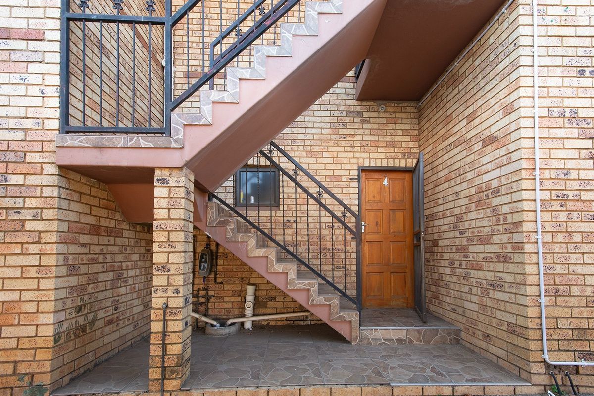 Exterior view of an apartment entrance featuring a face brick facade, external staircase with wrought iron balustrade, and a timber front door.