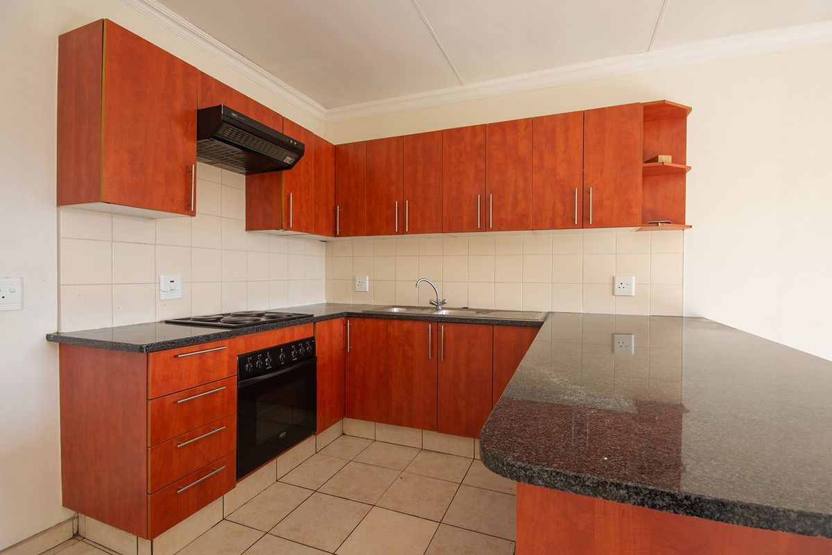 A functional kitchen featuring granite countertops, built-in oven, electric hob, extractor fan, and ample laminate cabinetry with a breakfast bar extension.
