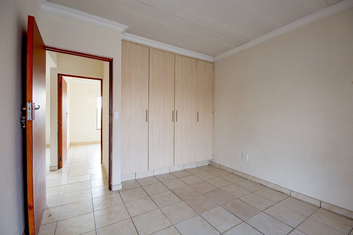 A clean, empty bedroom featuring neutral tiled flooring and built-in wooden cupboards, offering a blank canvas for personalization.