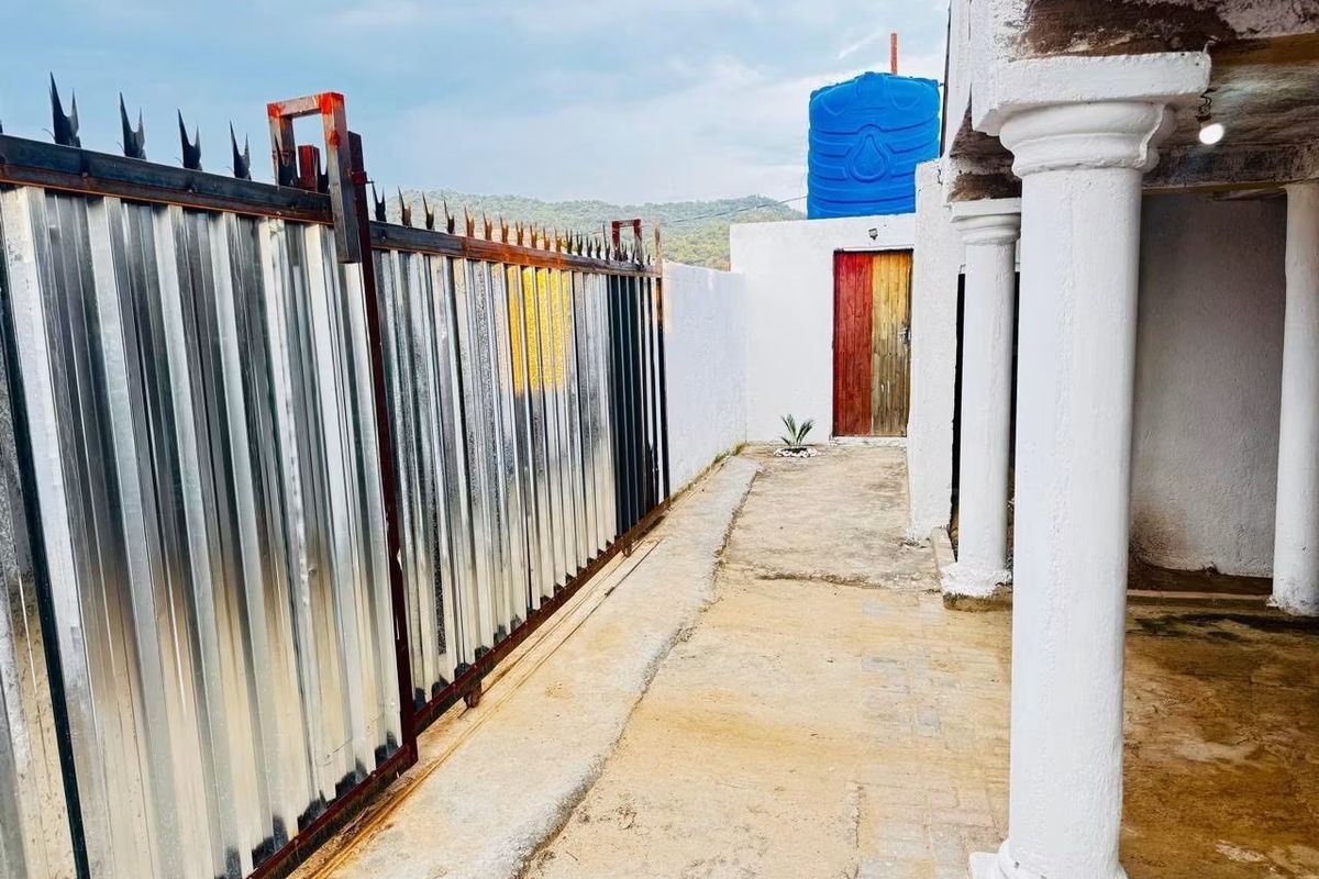 Rear exterior area featuring a corrugated metal gate, concrete columns, and a water storage tank on a concrete pathway.