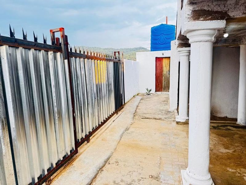 Rear exterior area featuring a corrugated metal gate, concrete columns, and a water storage tank on a concrete pathway.