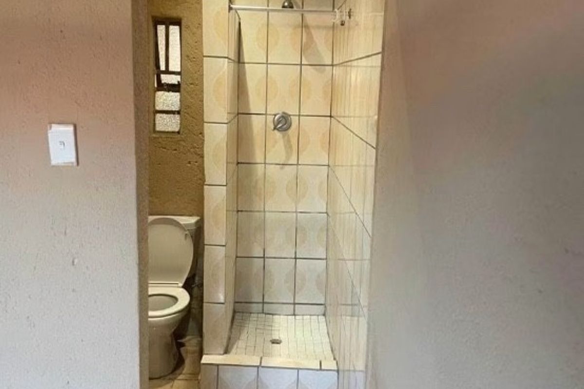 A compact bathroom featuring a tiled shower enclosure and a standard toilet, requiring cosmetic updates to modernize the dated finishes.