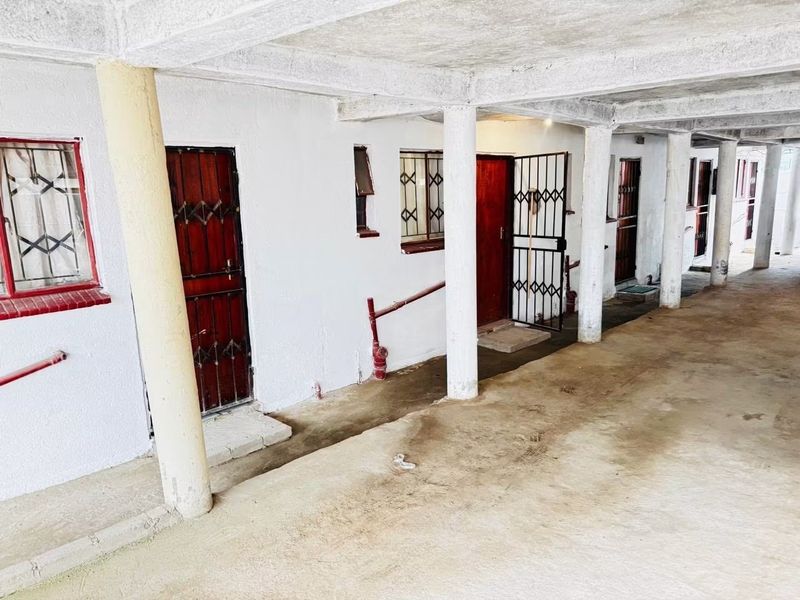 A covered outdoor walkway or patio area featuring concrete columns, security gates, and multiple access points to the building units.