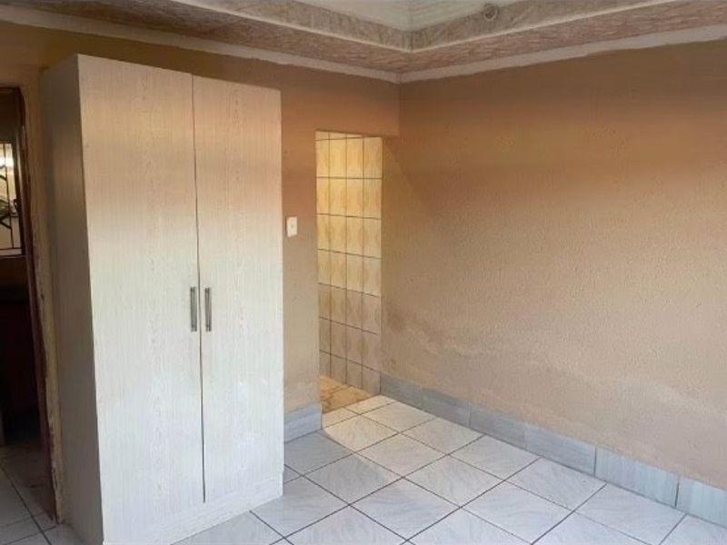 A bedroom featuring tiled flooring, a built-in wardrobe, and coved ceiling details, currently showing signs of wall moisture and staining.