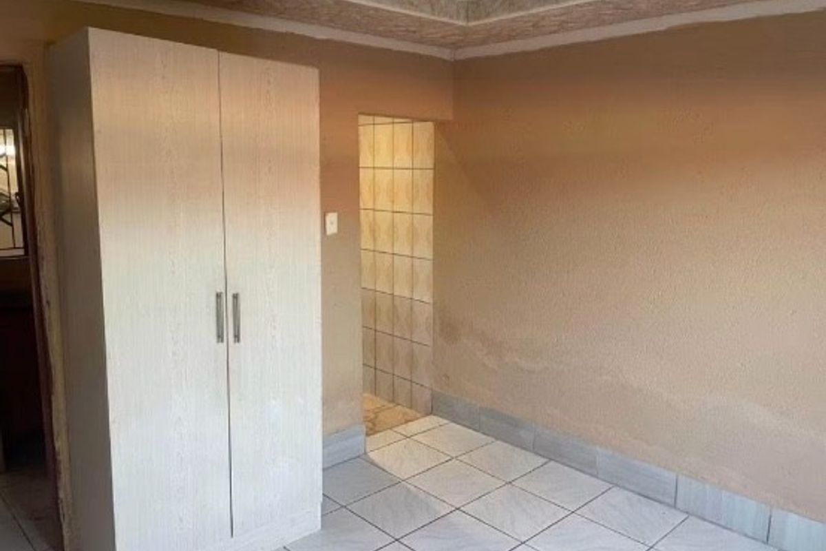 A bedroom featuring tiled flooring, a built-in wardrobe, and coved ceiling details, currently showing signs of wall moisture and staining.