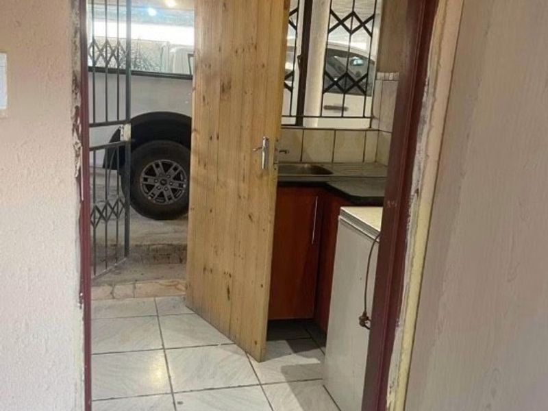 A small scullery or utility area featuring tiled floors, built-in cabinetry, and a sink, with direct access to the exterior via a security gate.