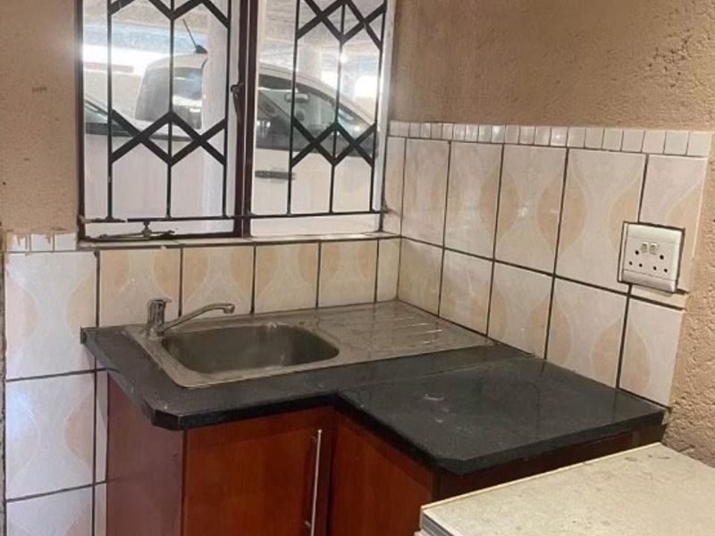 A compact kitchen area featuring a stainless steel sink, tiled splashback, and built-in cabinetry with a dark laminate countertop.