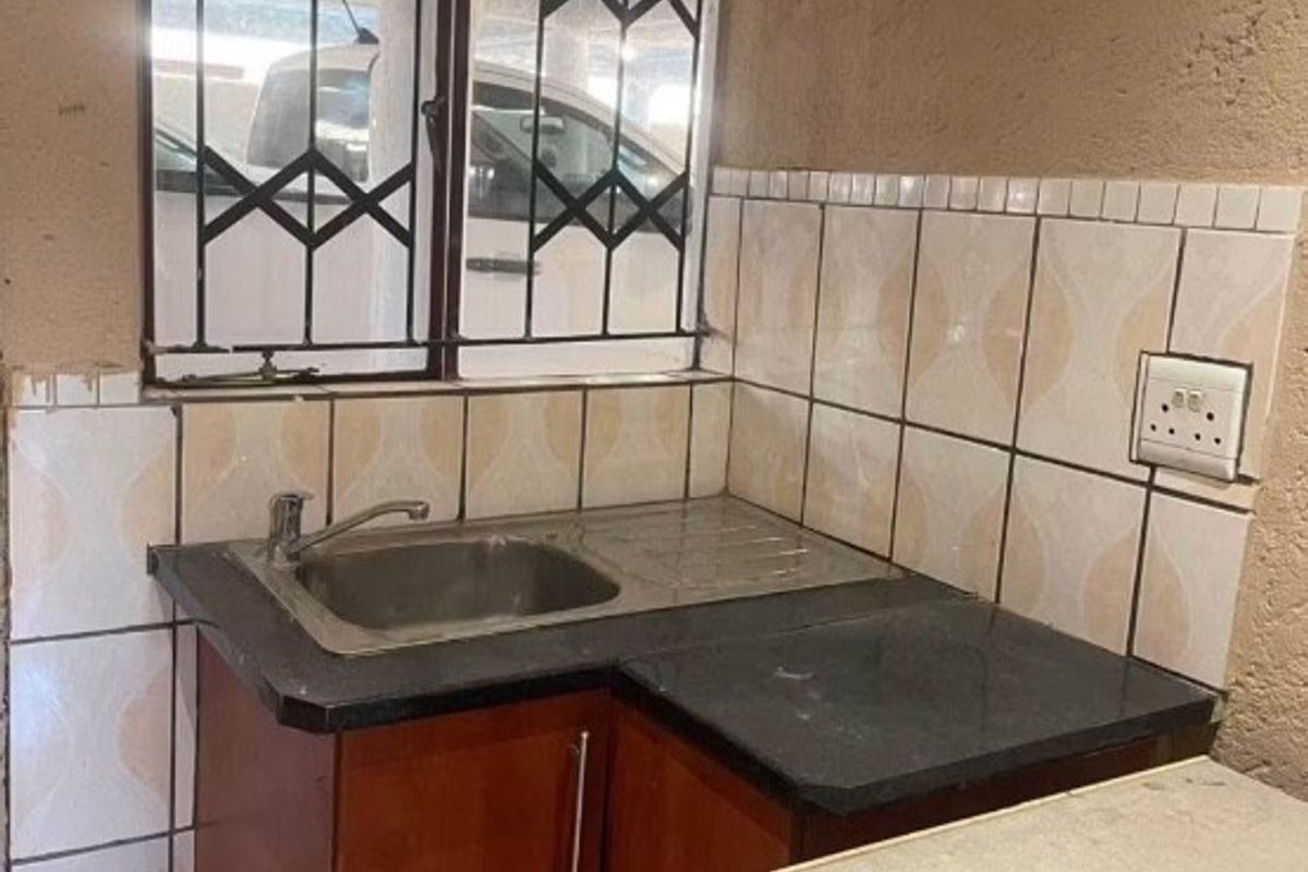A compact kitchen area featuring a stainless steel sink, tiled splashback, and built-in cabinetry with a dark laminate countertop.