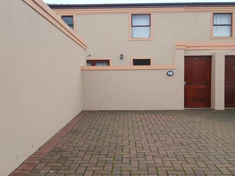 Front exterior view of the property featuring a paved driveway, boundary wall, and timber entrance doors to the units.