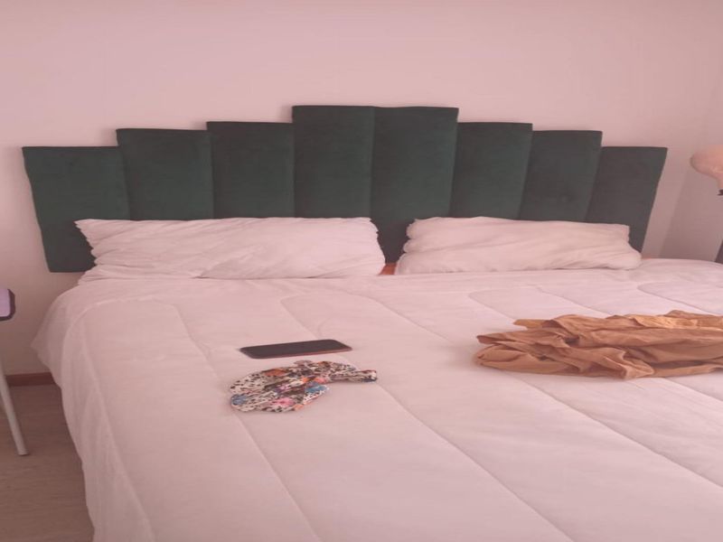A bedroom featuring light-toned laminate flooring and a dark green upholstered headboard.