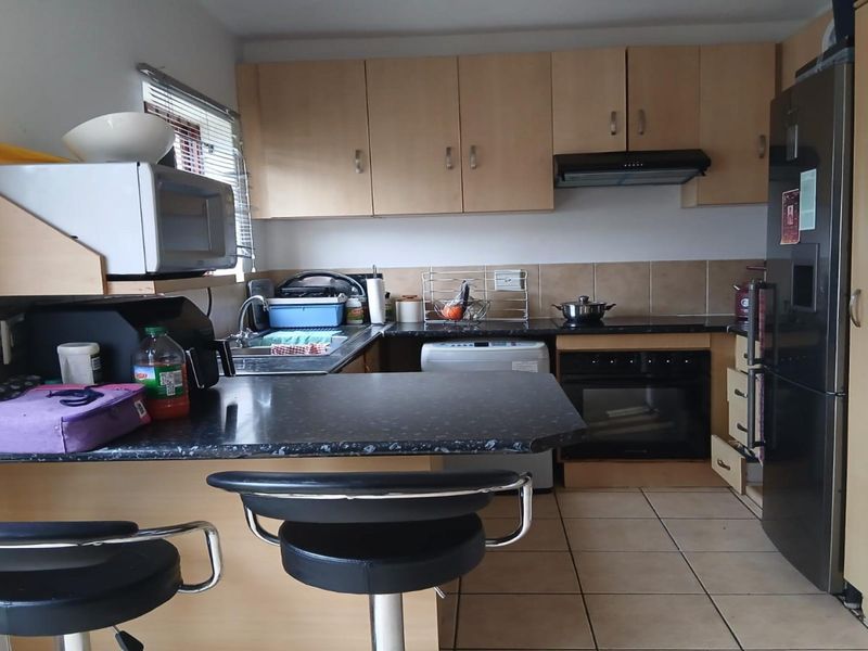 A functional kitchen featuring laminate cabinetry, dark countertops, built-in oven, extractor fan, and tiled flooring with a breakfast bar area.