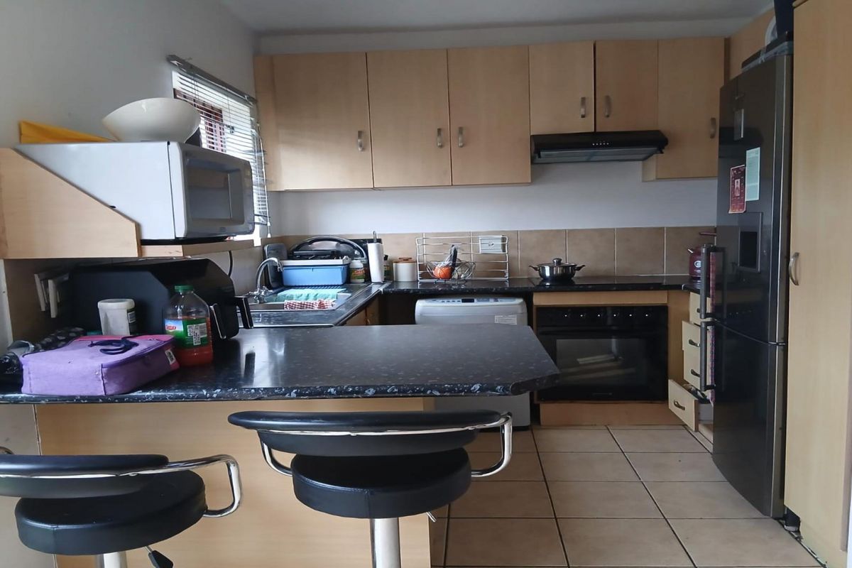 A functional kitchen featuring laminate cabinetry, dark countertops, built-in oven, extractor fan, and tiled flooring with a breakfast bar area.