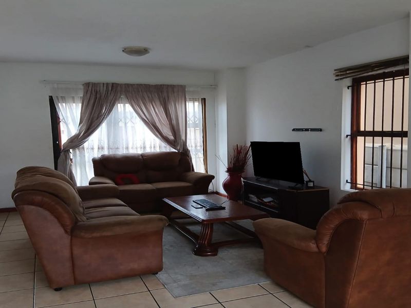 A spacious living room featuring neutral tiled flooring, large windows with security bars, and ample natural light.