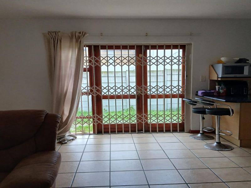 Open plan living area featuring tiled flooring and timber framed sliding doors with security gate, leading to an outdoor space.