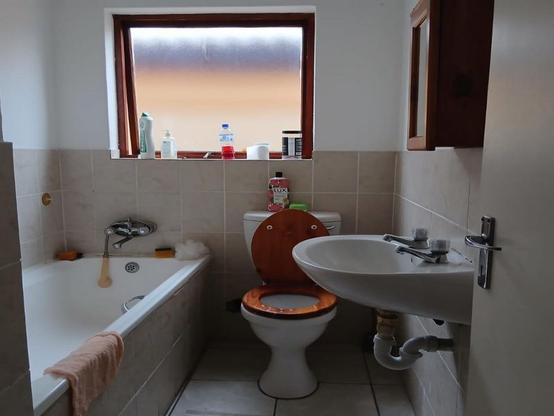 A functional bathroom featuring a bathtub, pedestal basin, and toilet with neutral wall and floor tiling.