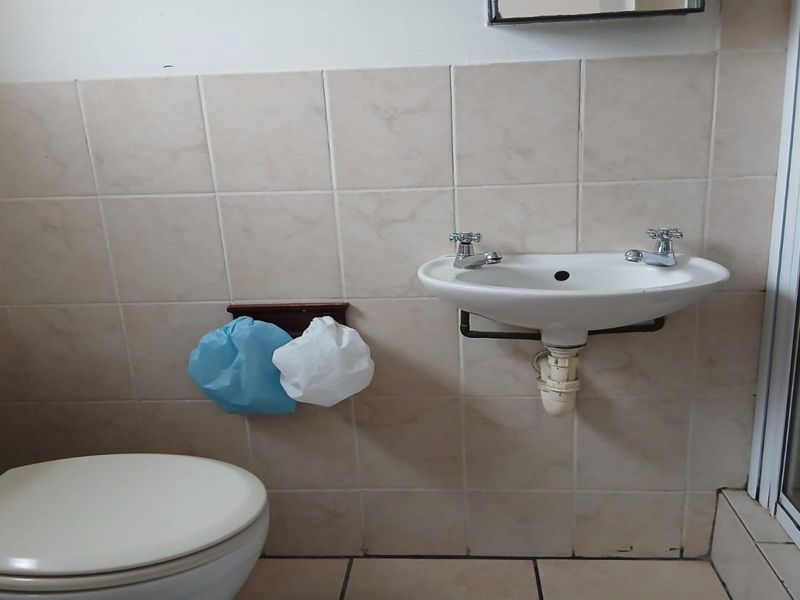 A functional bathroom featuring a wall-mounted basin, toilet, and shower enclosure with neutral ceramic wall and floor tiling.