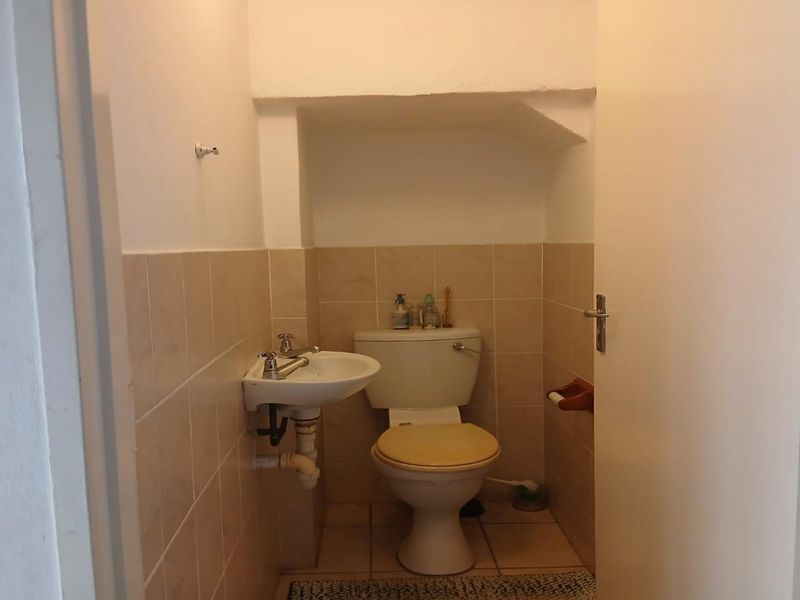 A functional guest bathroom featuring a wall-mounted basin and standard toilet with neutral ceramic wall and floor tiling.