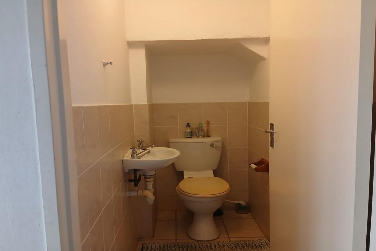 A functional guest bathroom featuring a wall-mounted basin and standard toilet with neutral ceramic wall and floor tiling.