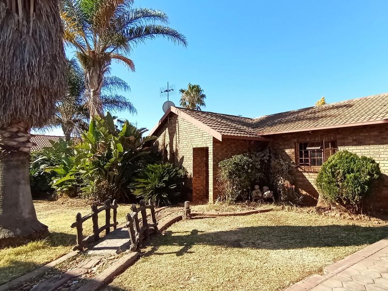 A front view of a face-brick house featuring a tiled roof, paved driveway, and a landscaped garden with a decorative bridge.