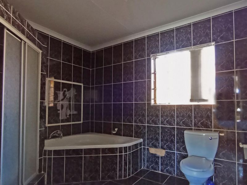 A dated bathroom featuring dark marble-effect wall tiles, a corner bathtub, a shower enclosure, and a toilet, requiring cosmetic updates.