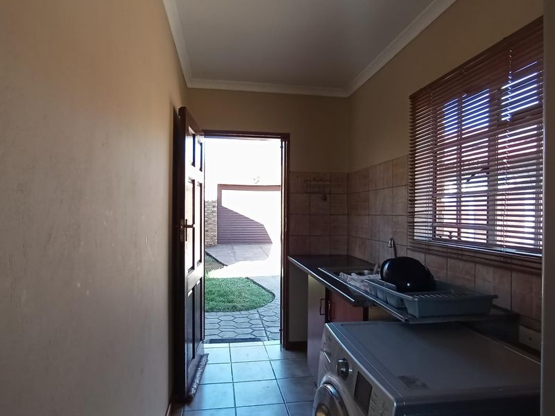 A functional laundry area featuring tiled flooring, a sink with a tiled splashback, and direct access to the exterior.