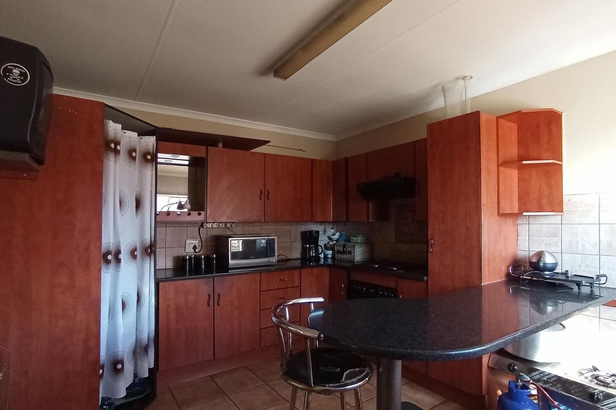 A functional kitchen featuring wood-look cabinetry, dark laminate countertops, tiled backsplash, and integrated cooking appliances, offering a practical layout for daily use.